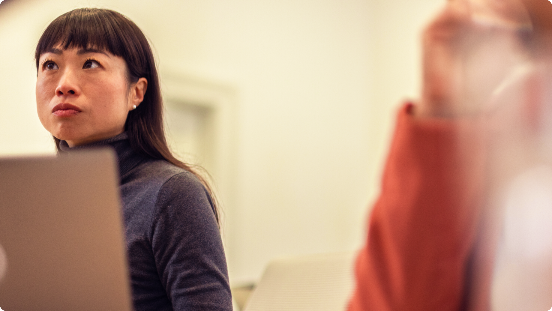 Woman holding a laptop looks up thoughtfully in a bright office.