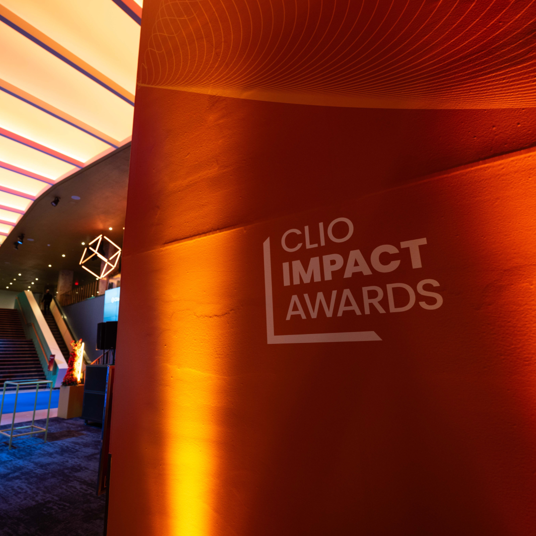 CLIO IMPACT AWARDS logo on an orange illuminated wall in a modern event venue.