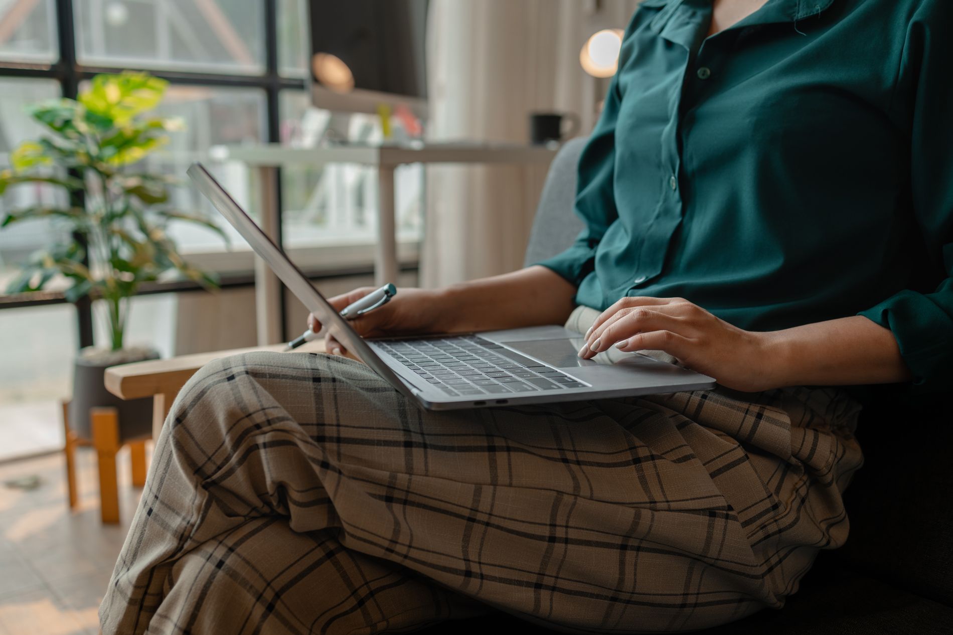 Person in a green shirt and plaid pants using a laptop.