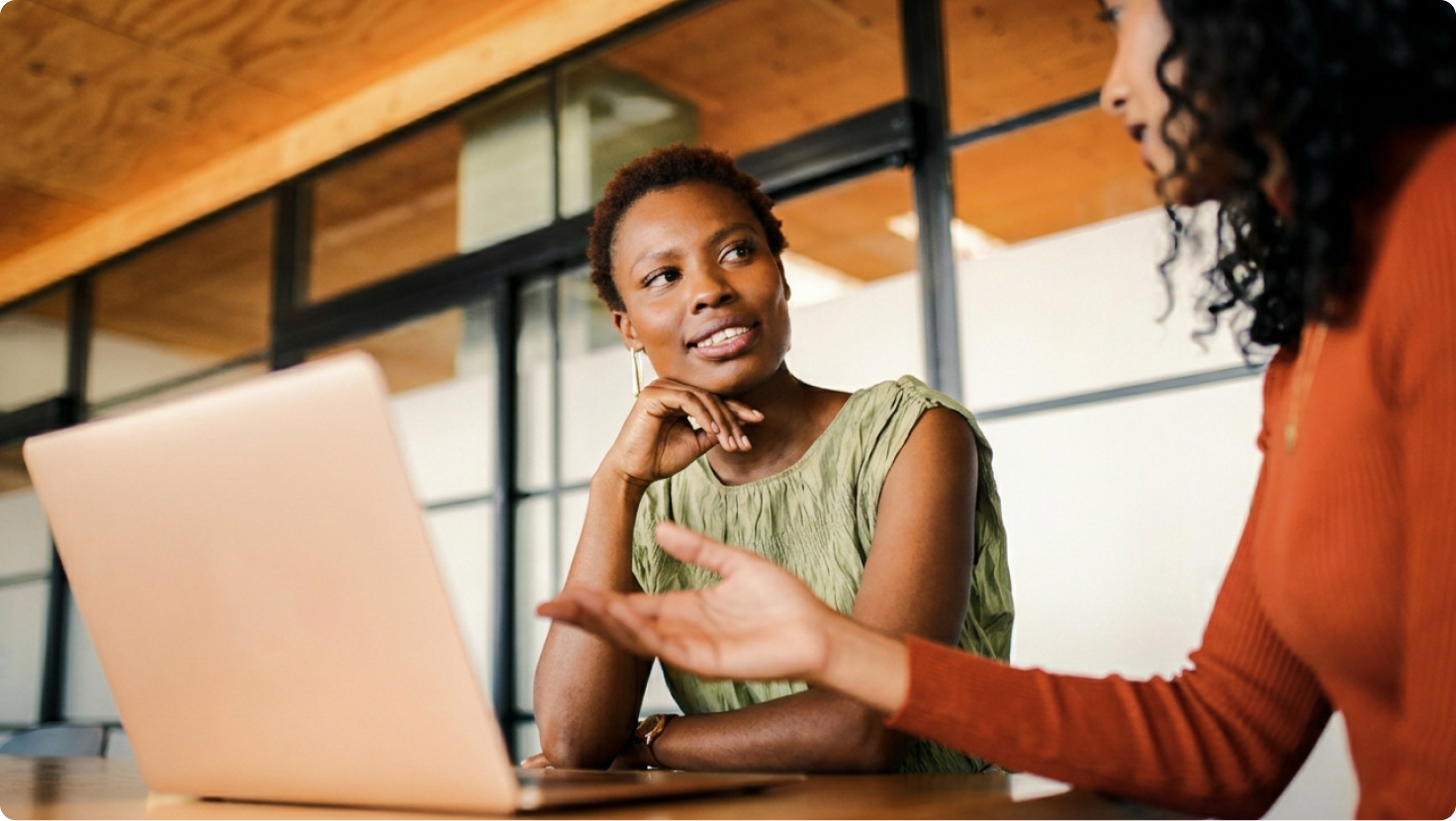 Two women engaged in a discussion, with a laptop on the table.