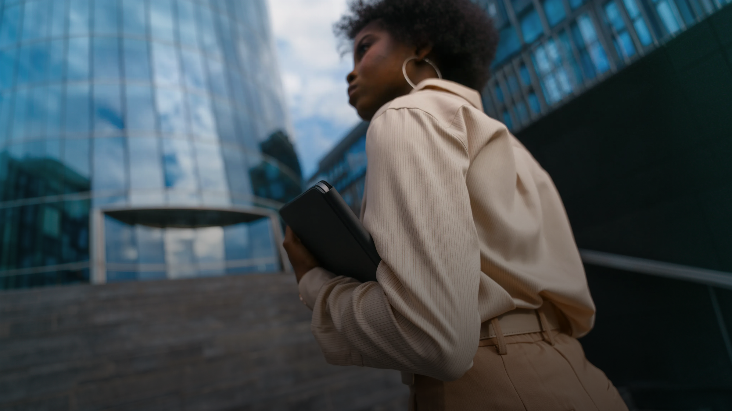 Young woman holding a tablet walks past a modern glass building.