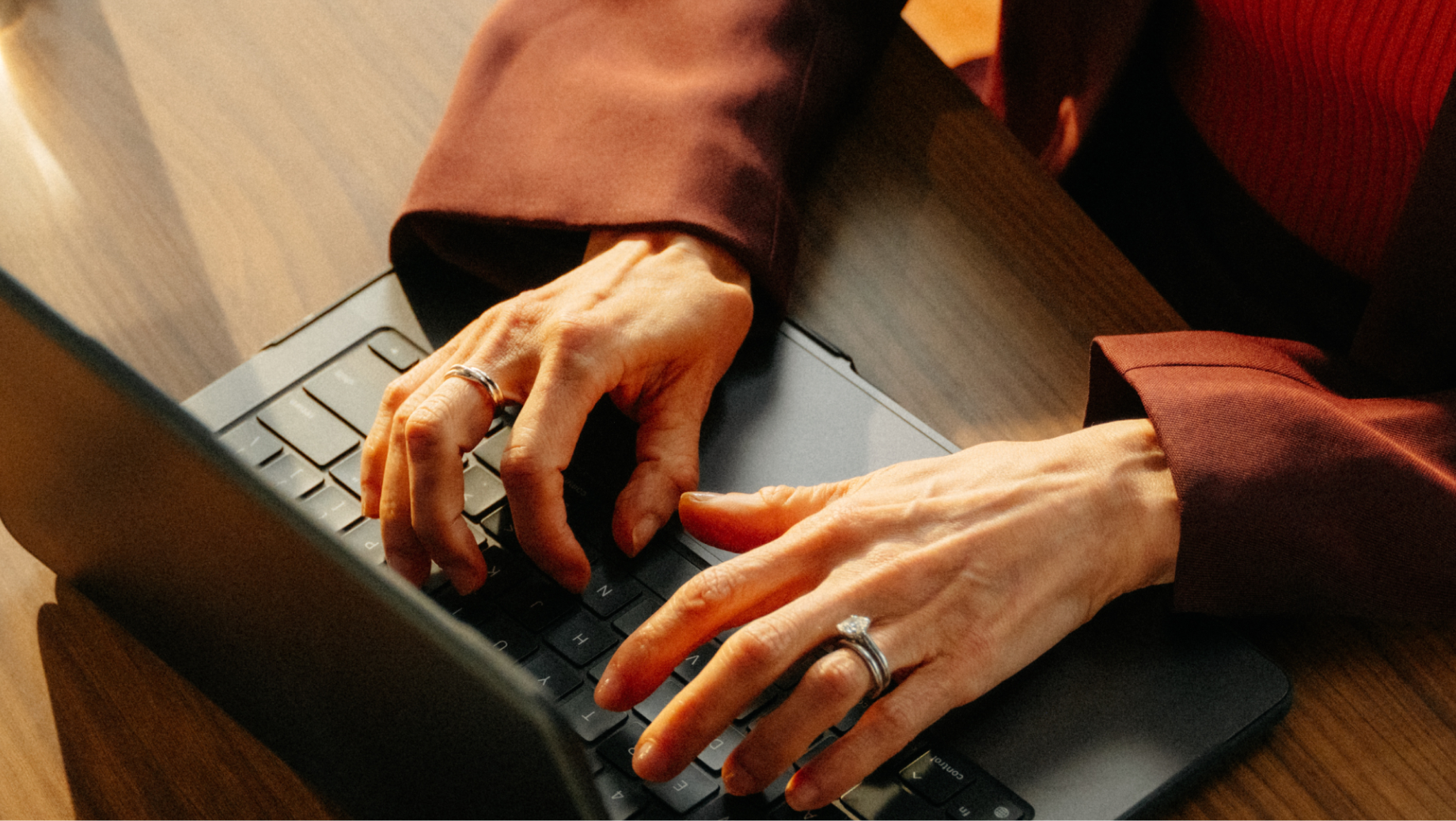 Hands typing on a laptop keyboard at a wooden desk.