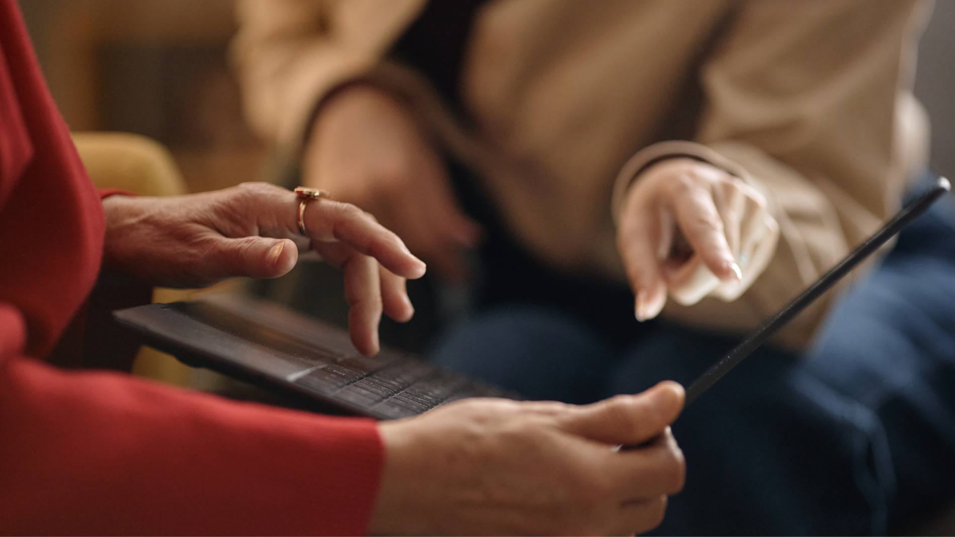 Two people's hands interacting with a tablet, one typing and the other pointing.