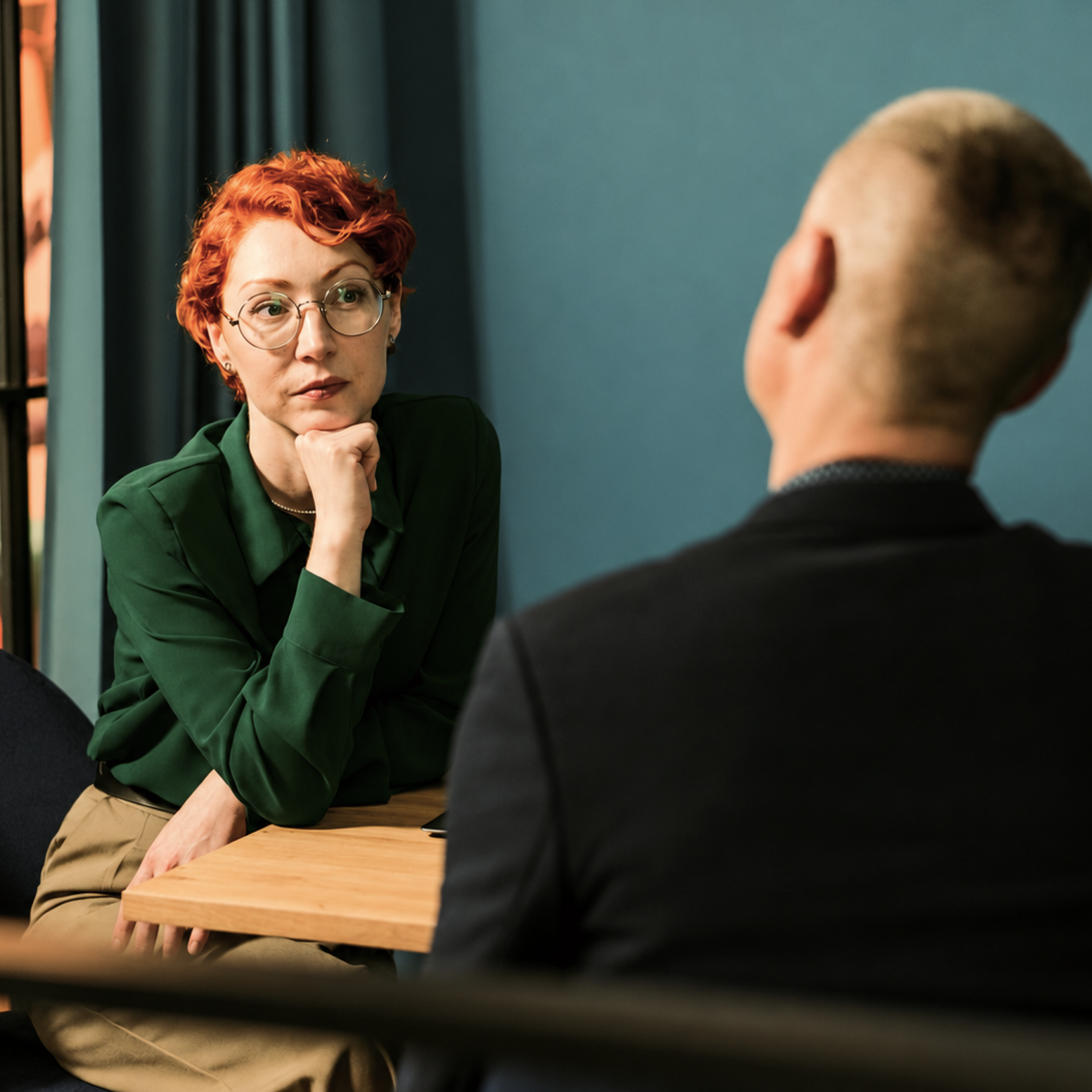 A woman in glasses listens closely across a table during a meeting with a colleague.