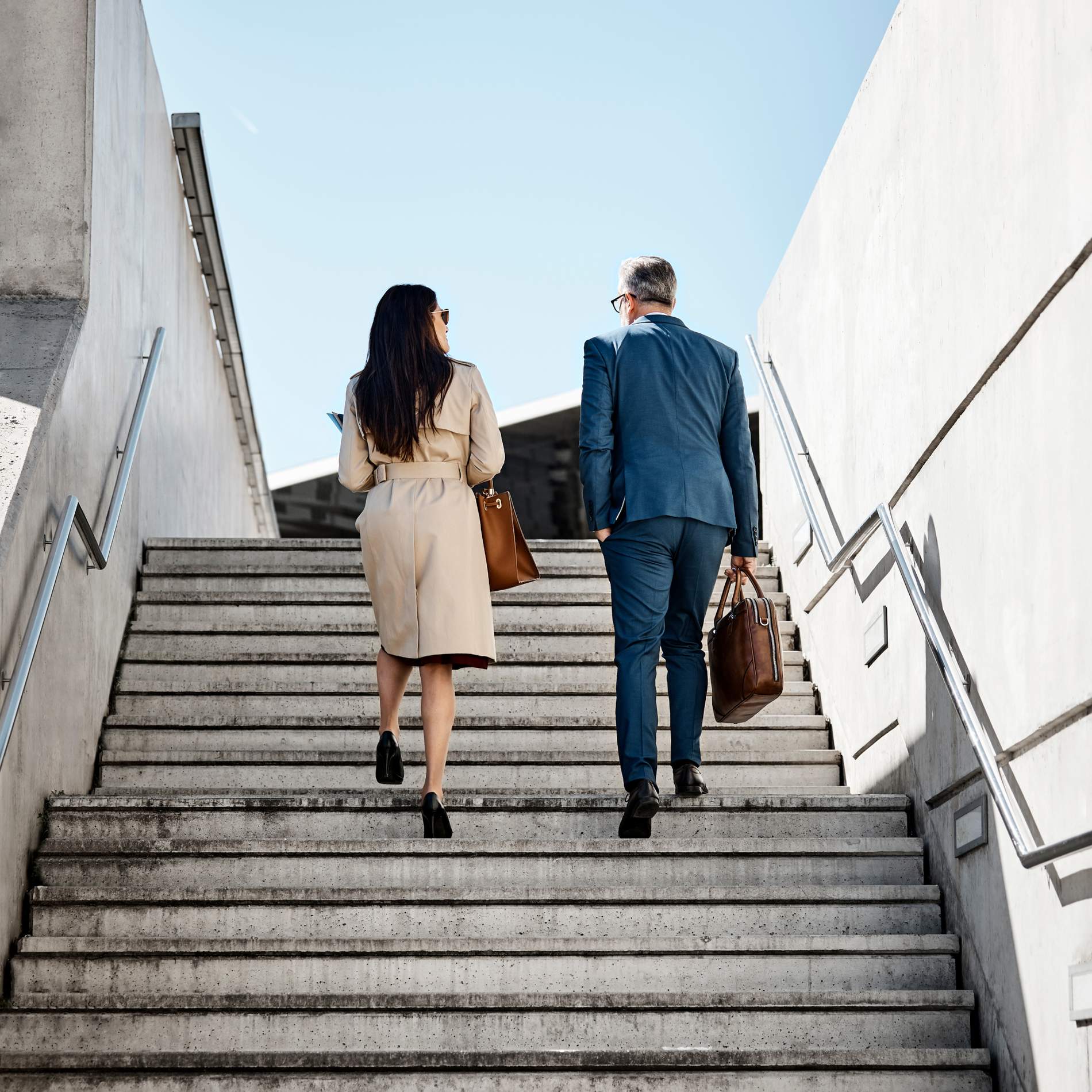 Two business people walking up concrete stairs from behind.