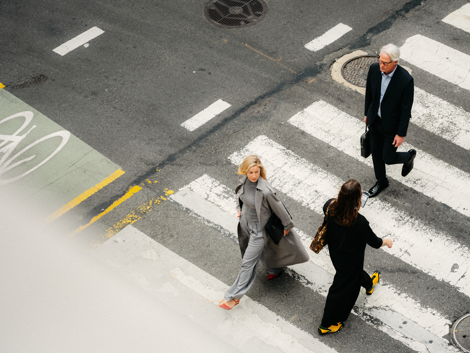 Overhead view of three people crossing a street on a crosswalk.