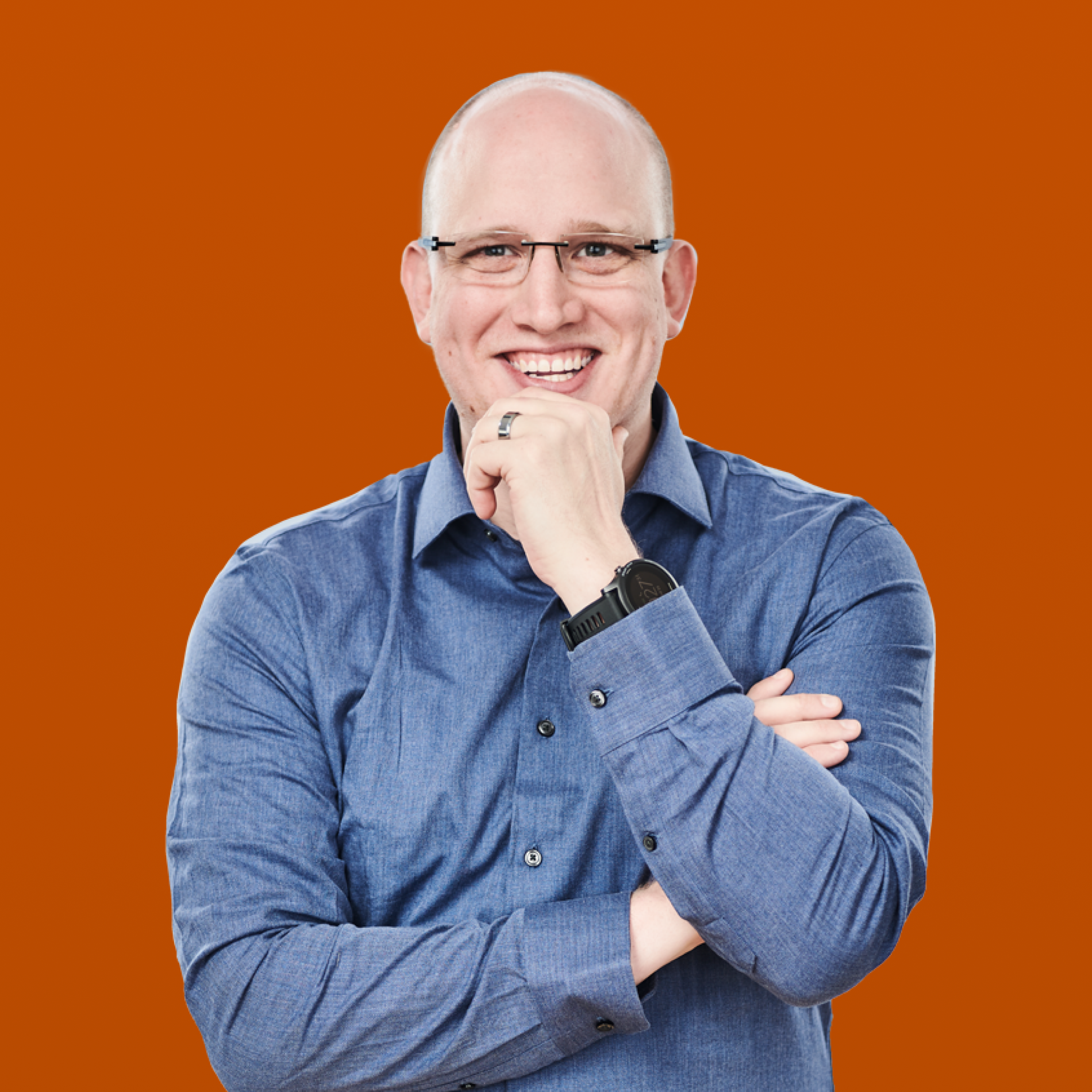 Smiling bald man in glasses and a blue shirt, hand on chin, against an orange background.