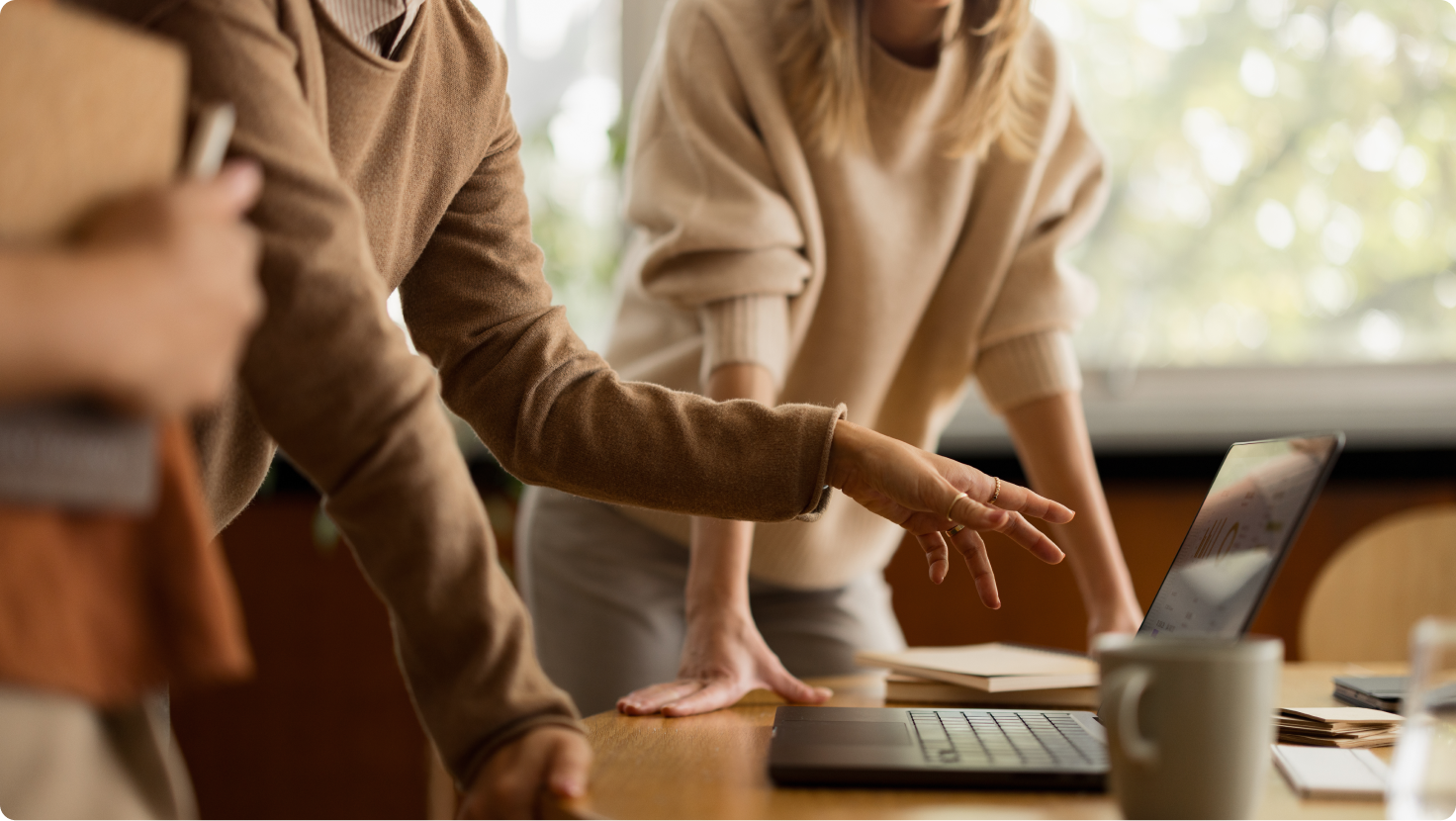 Two people collaborating, one pointing at a laptop on a wooden desk.