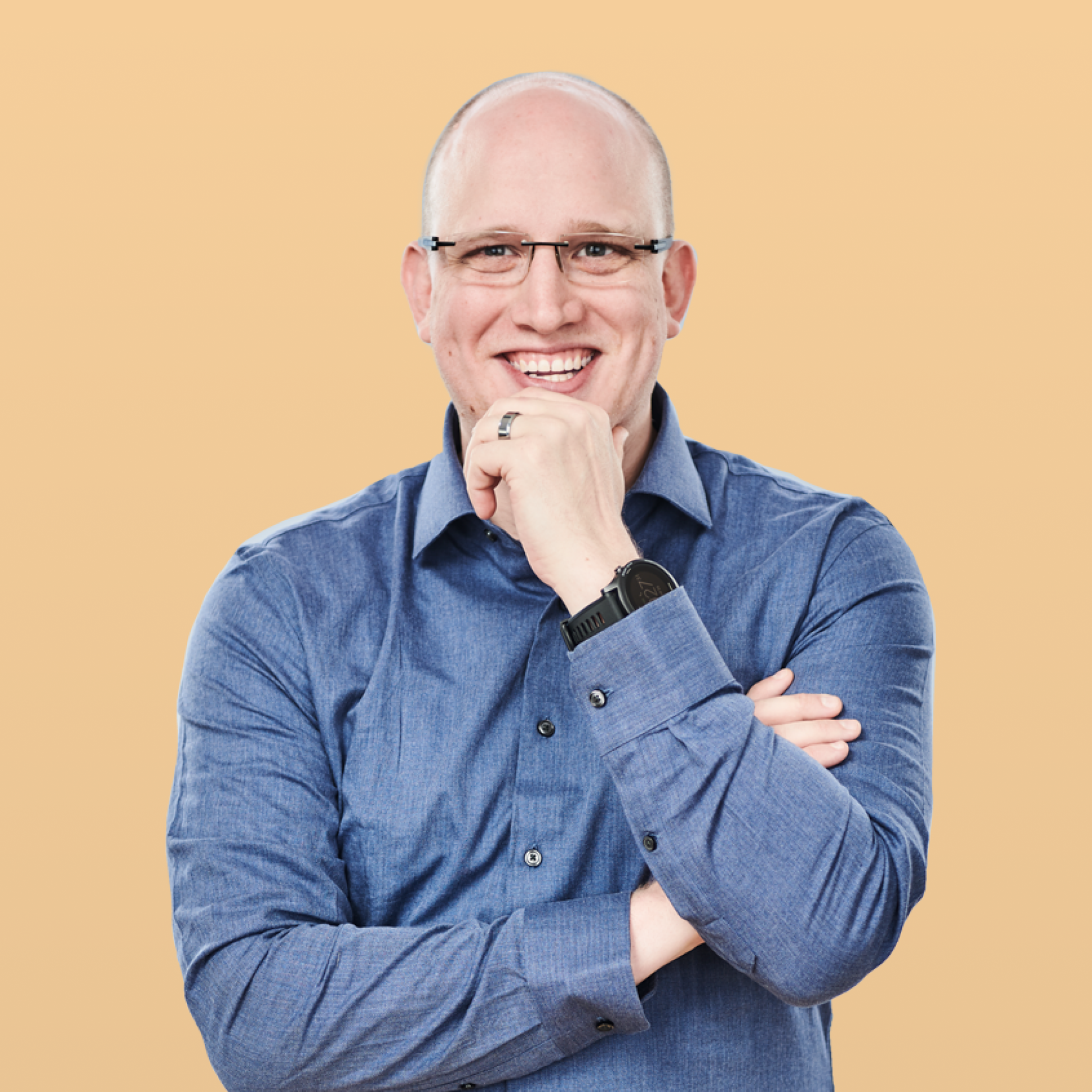 Smiling bald man with glasses in a blue shirt, hand on chin.
