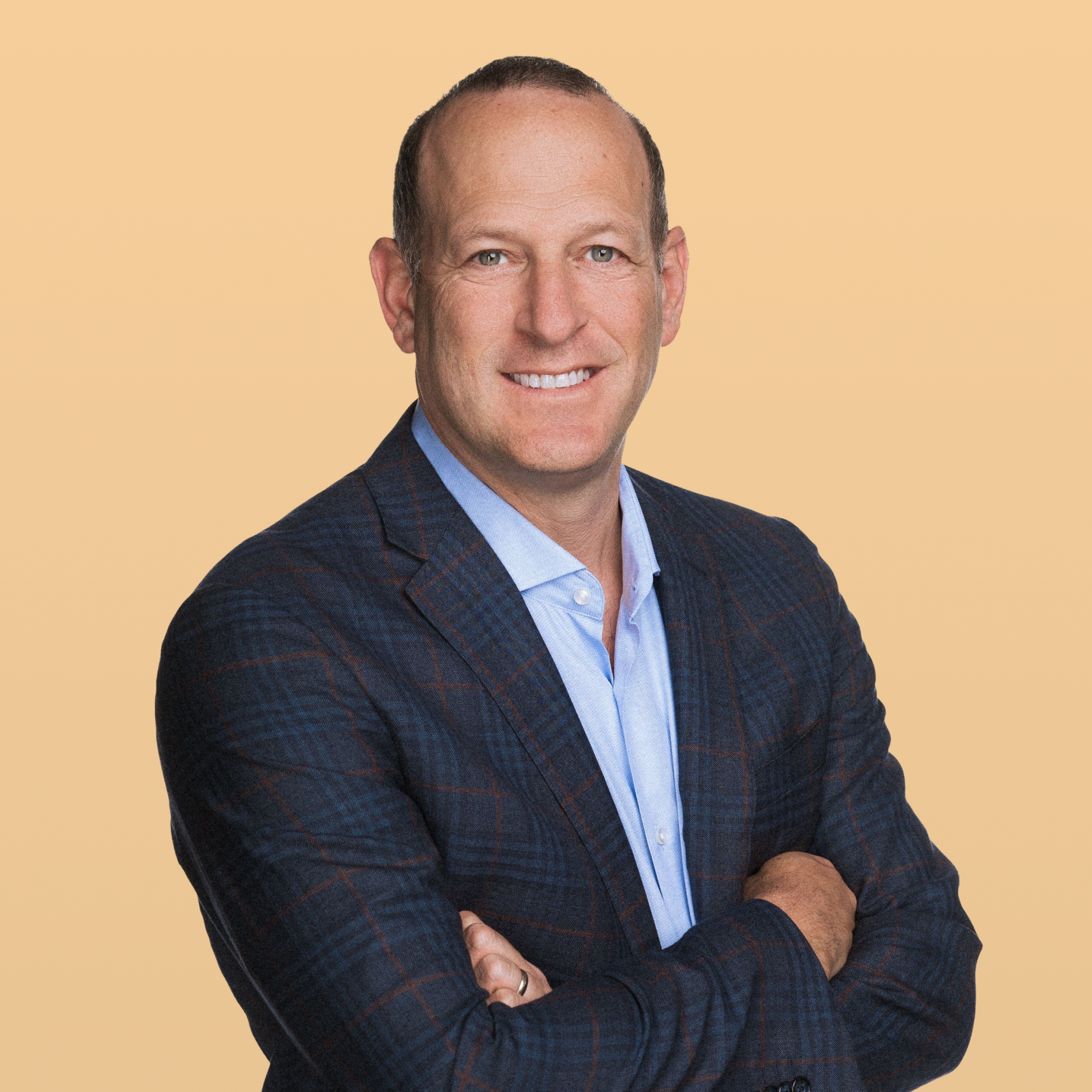 Smiling man in a blue plaid suit jacket with arms crossed.