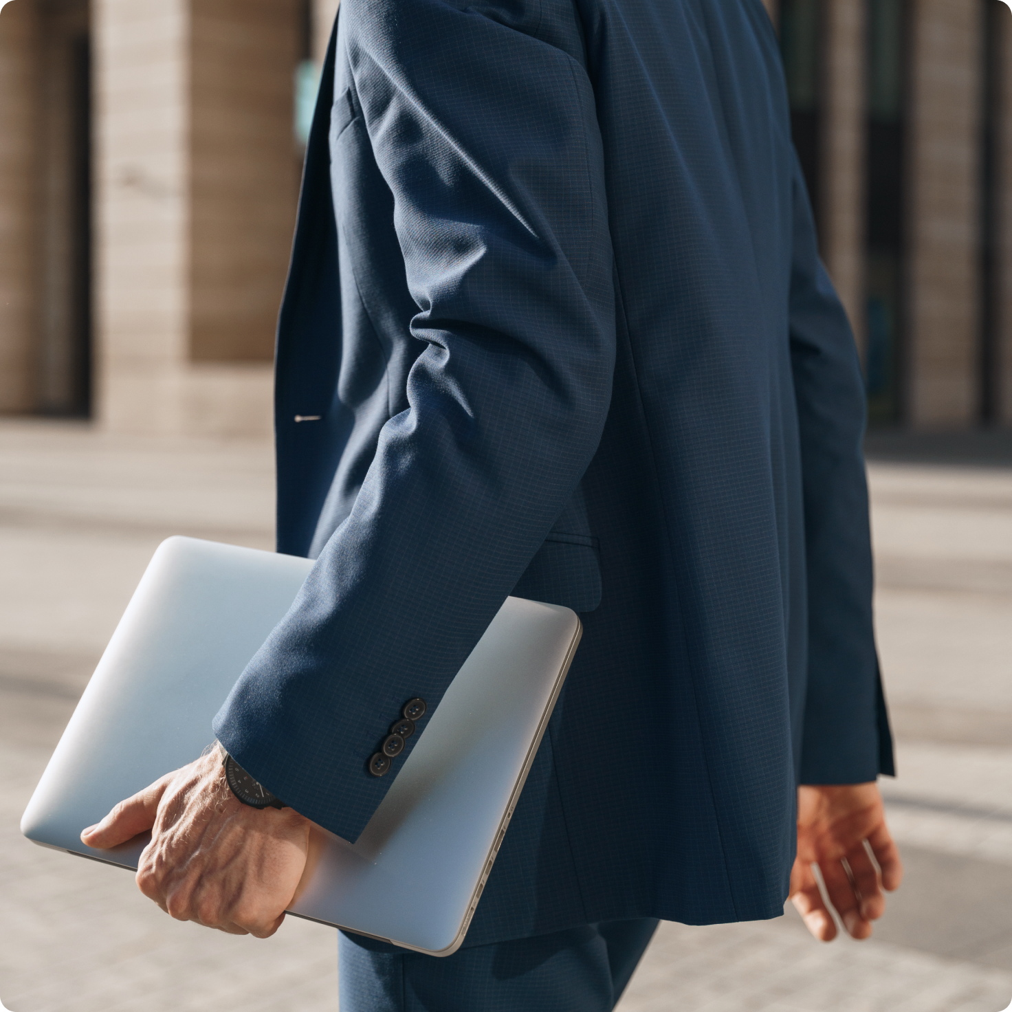 A person in a blue suit holds a silver laptop while walking.