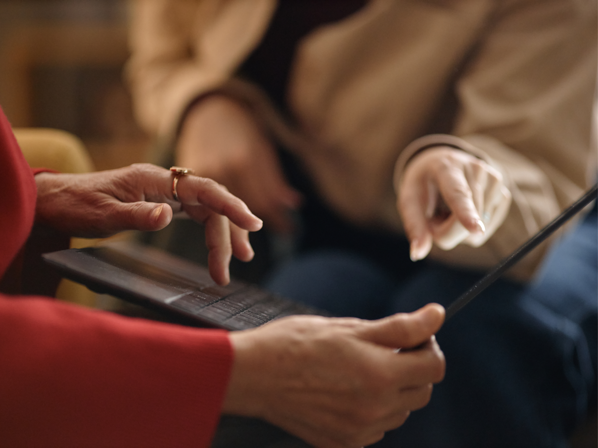 Hands of two people, one typing on a laptop and another pointing at its screen.