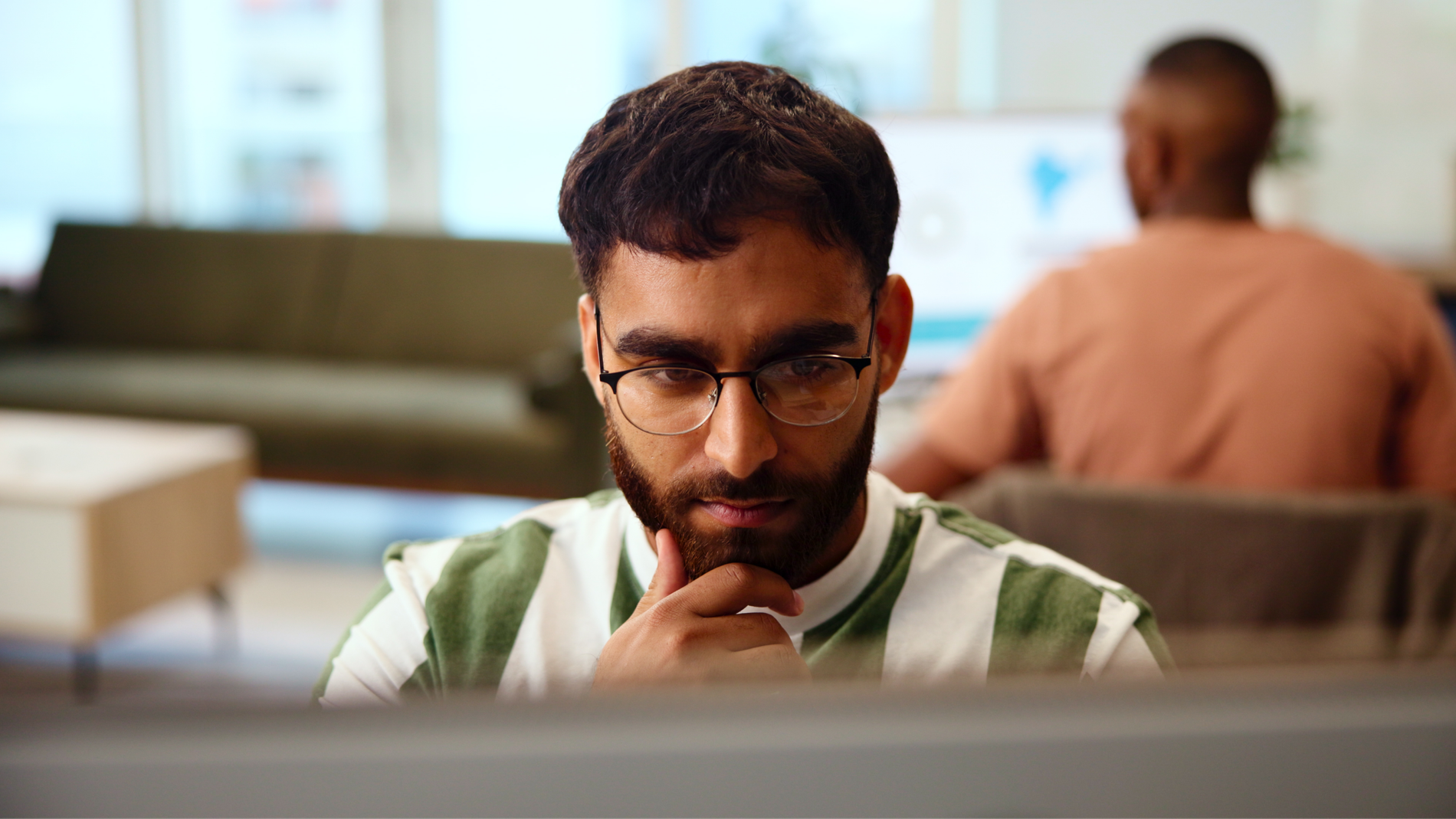 Man with glasses and beard looking intently at a screen, hand on chin.