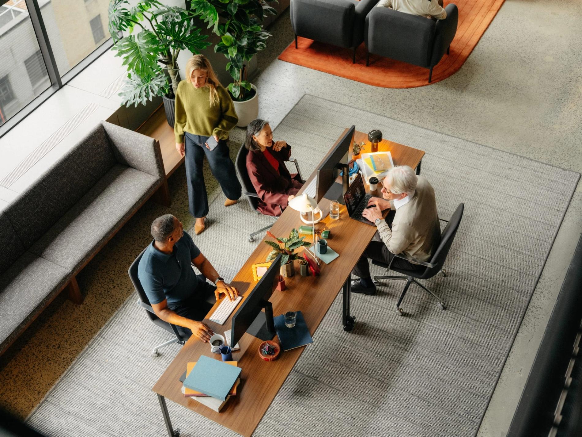 Overhead view of colleagues working at a shared desk in an open office.