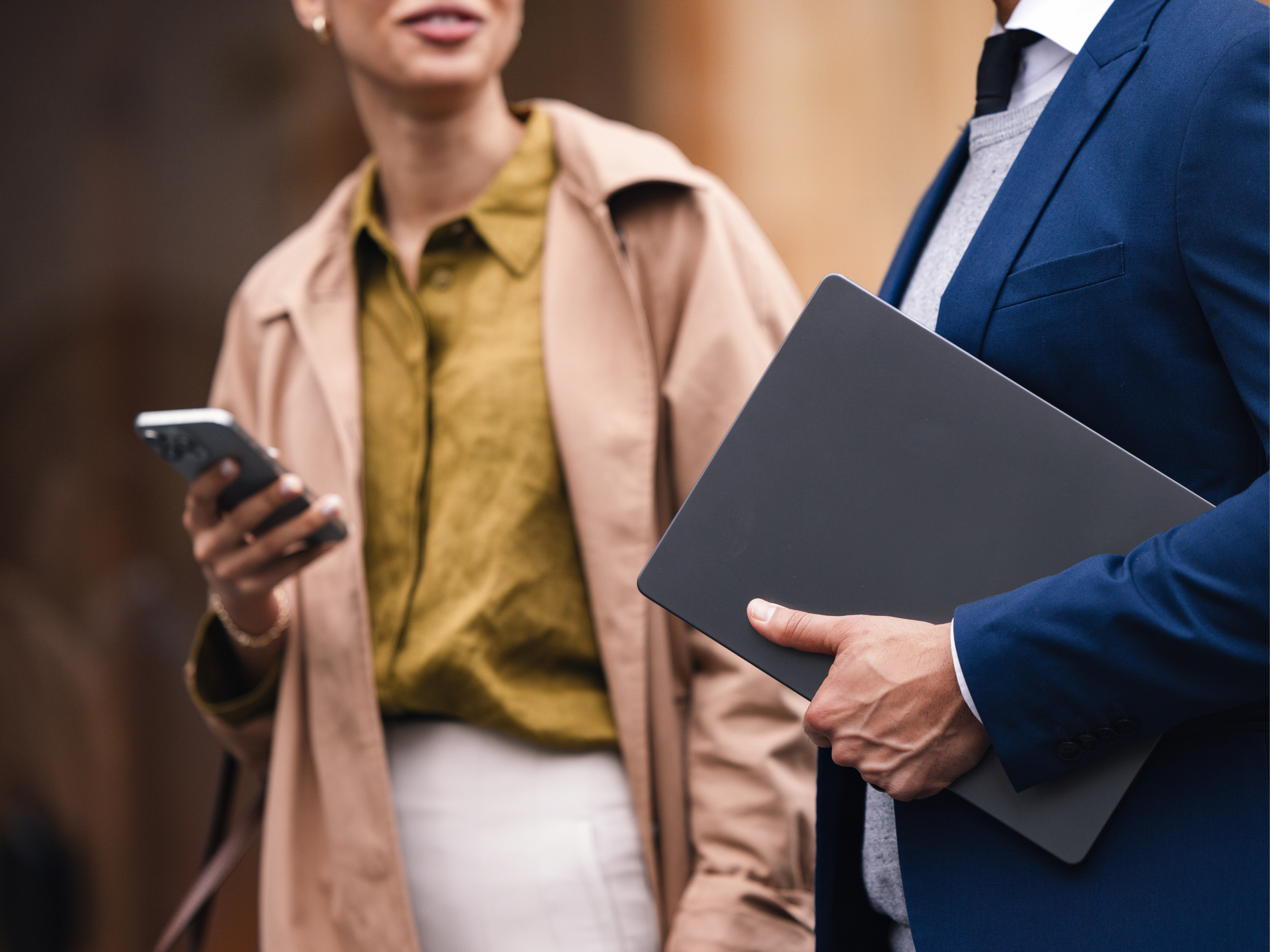 Professionally dressed woman on phone next to man holding laptop.