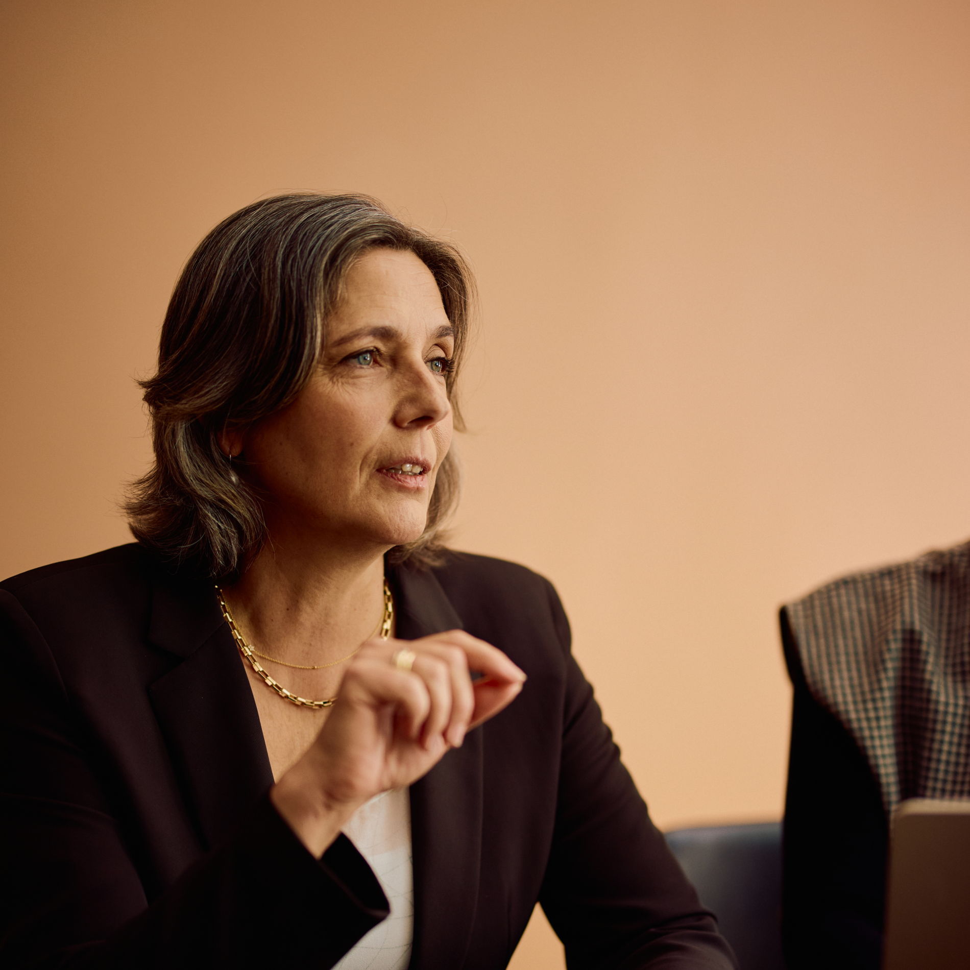 A senior professional in a dark blazer speaking during a meeting.
