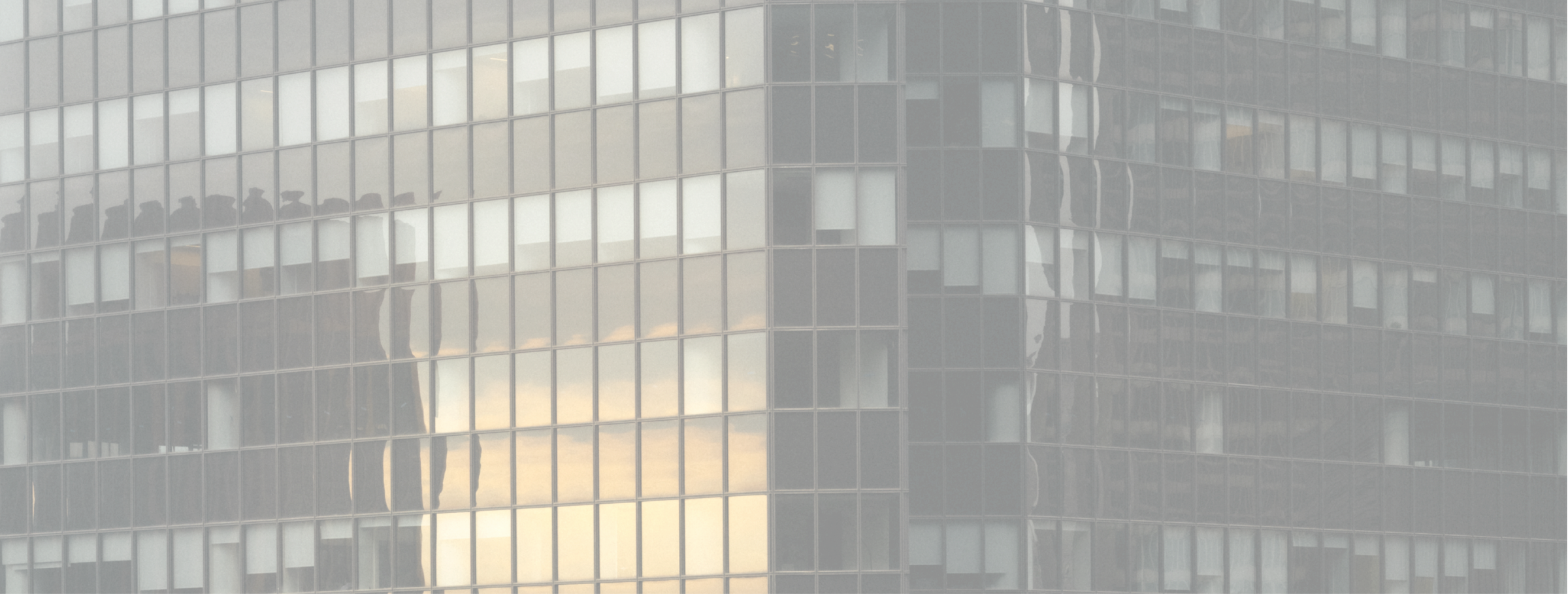 Facade of a modern building with reflective glass windows showing a golden sky reflection.