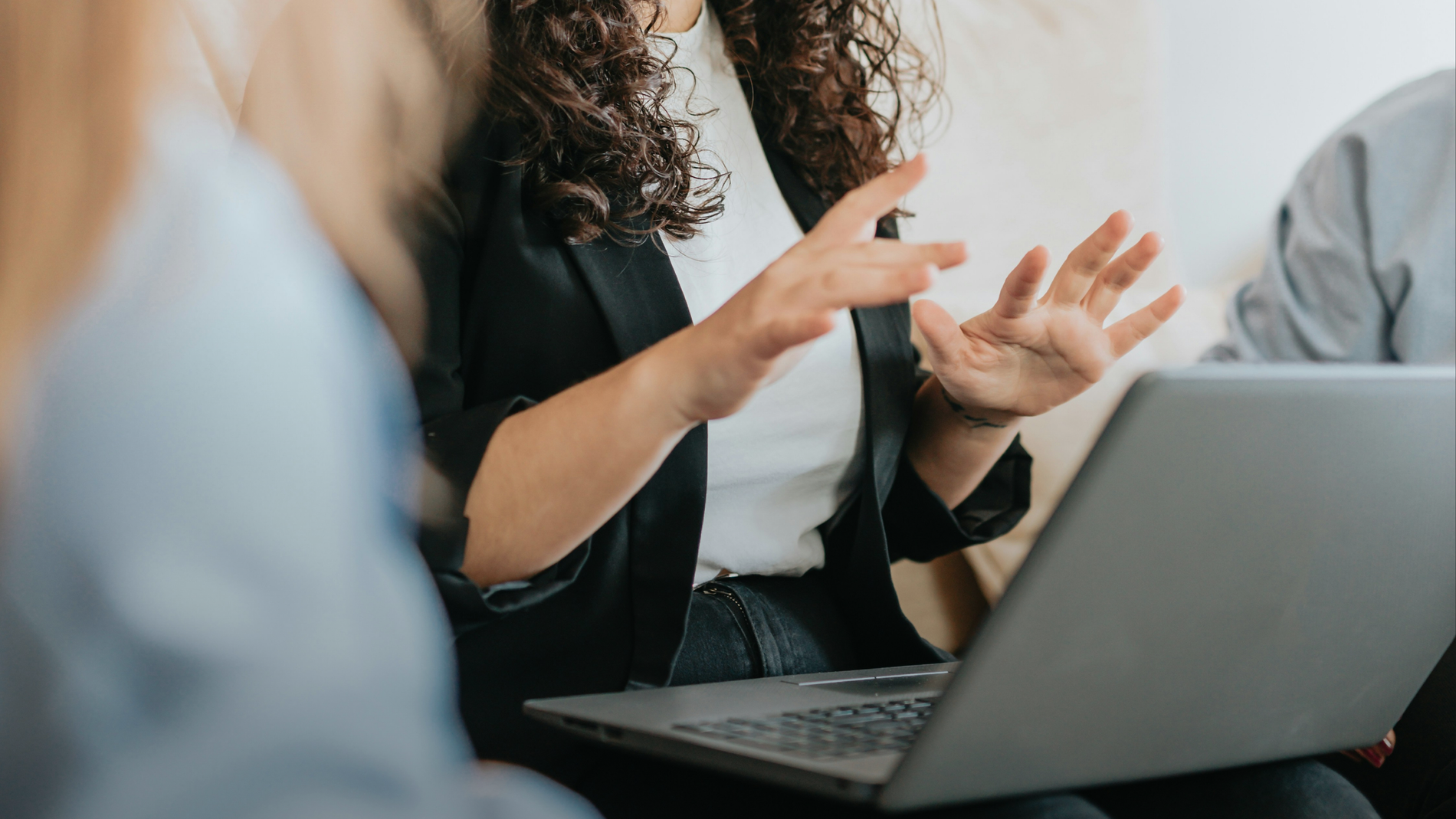 Curly-haired person gesturing over a laptop.