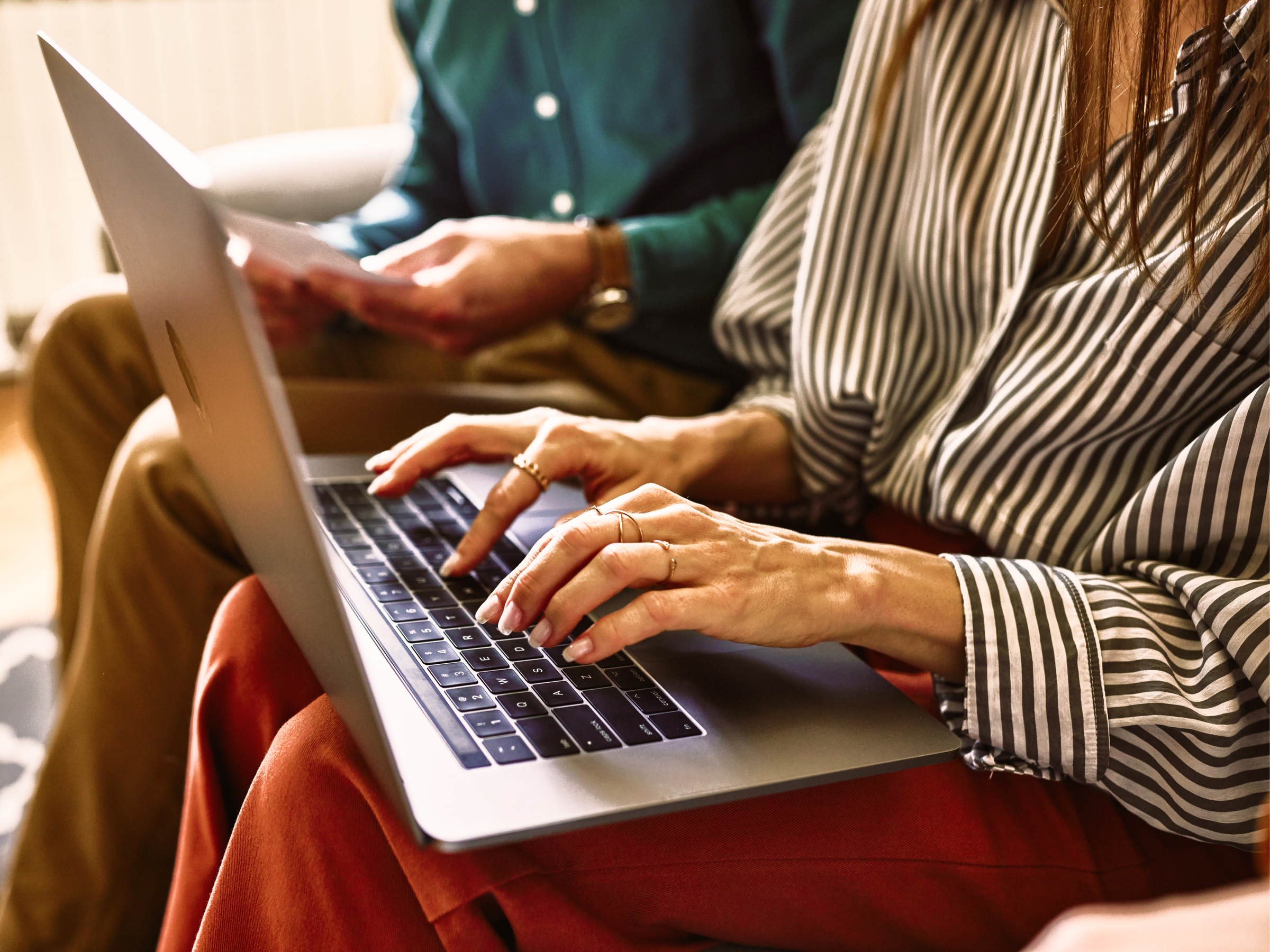 Woman typing on a laptop, with another person in the background.