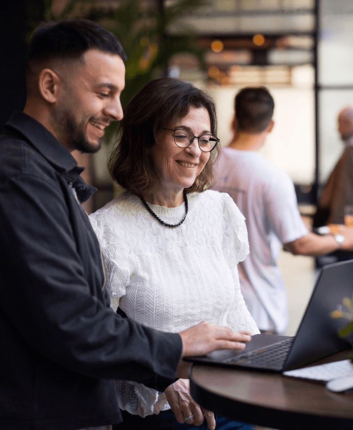 Two smiling people looking at a laptop together, with the man pointing at the screen.