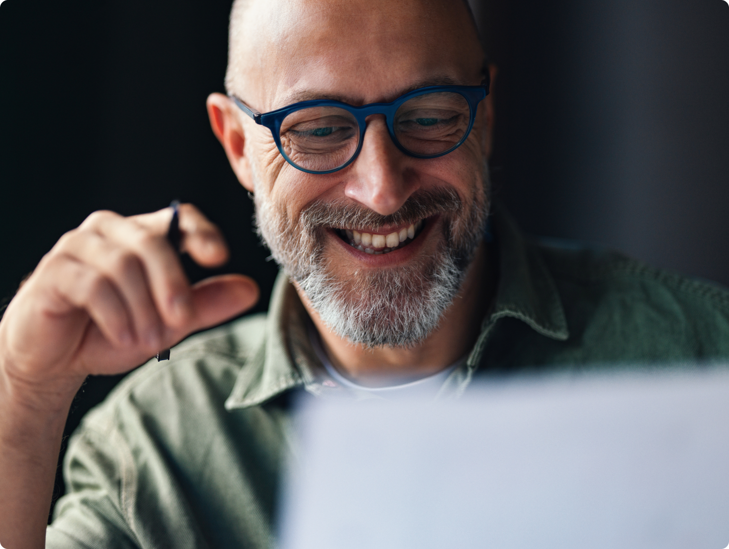 Smiling man with grey beard and blue glasses looking at a document.