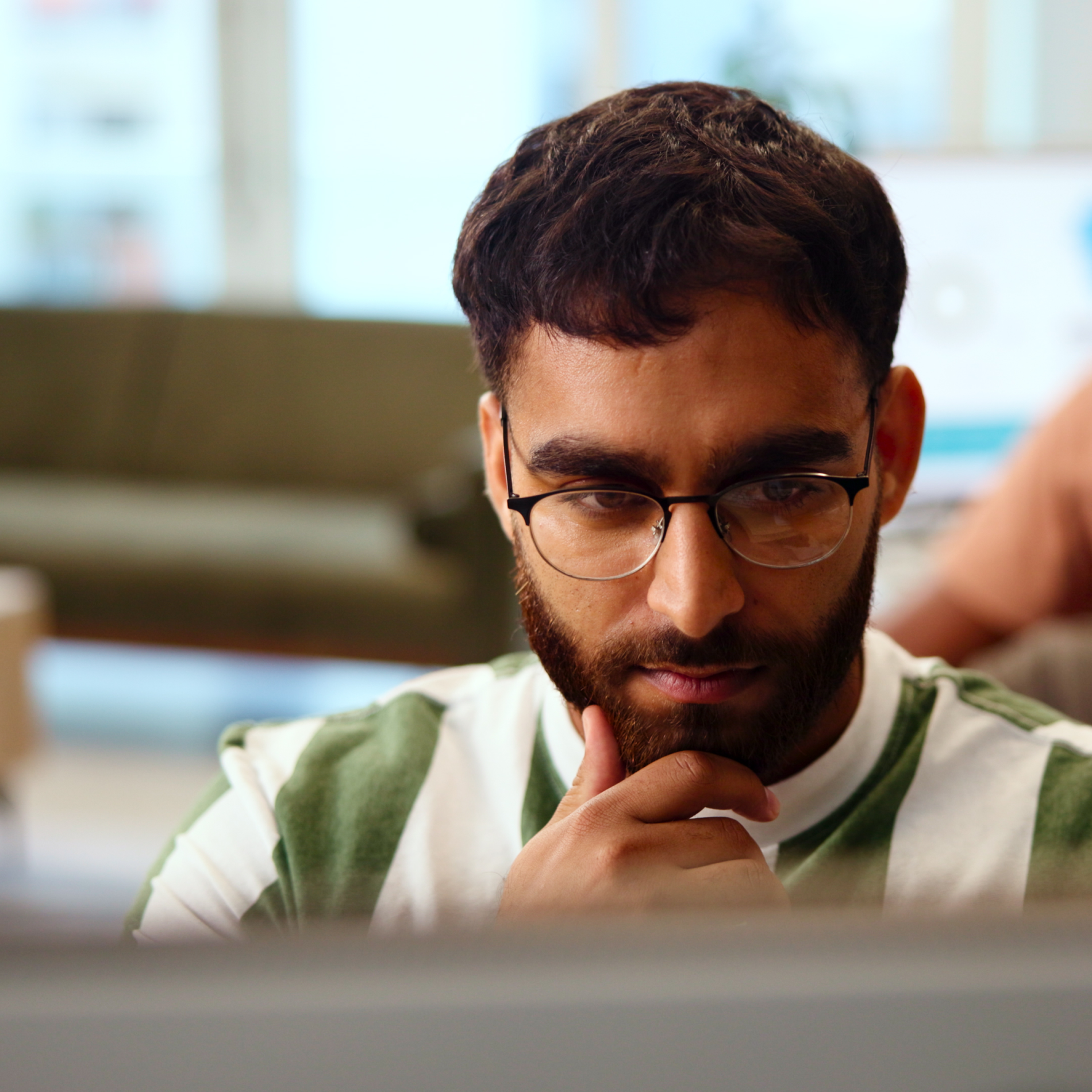 Man with a beard and glasses looking intently downwards, hand on chin.