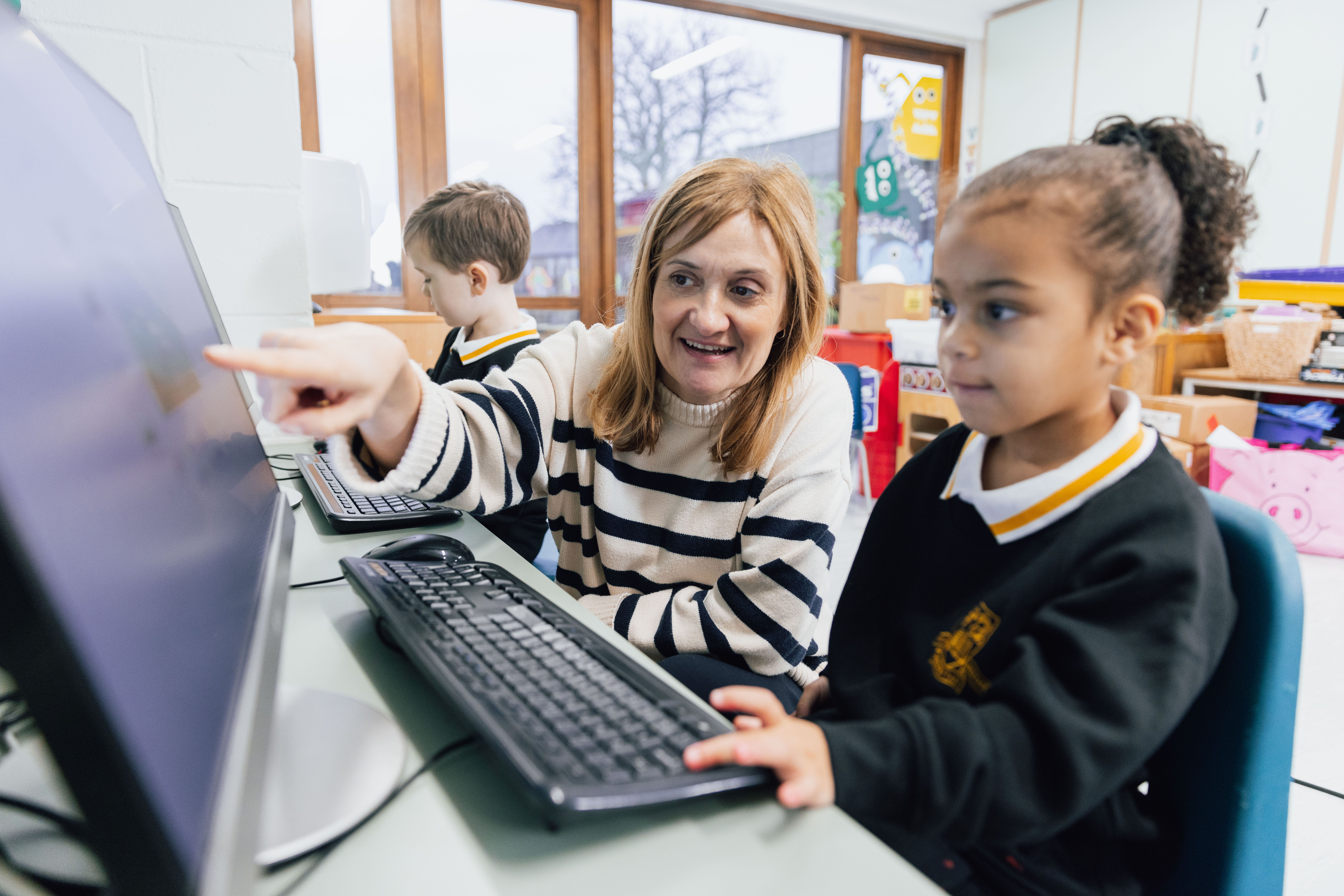 Image of a woman in between two children, pointing to a computer screen 