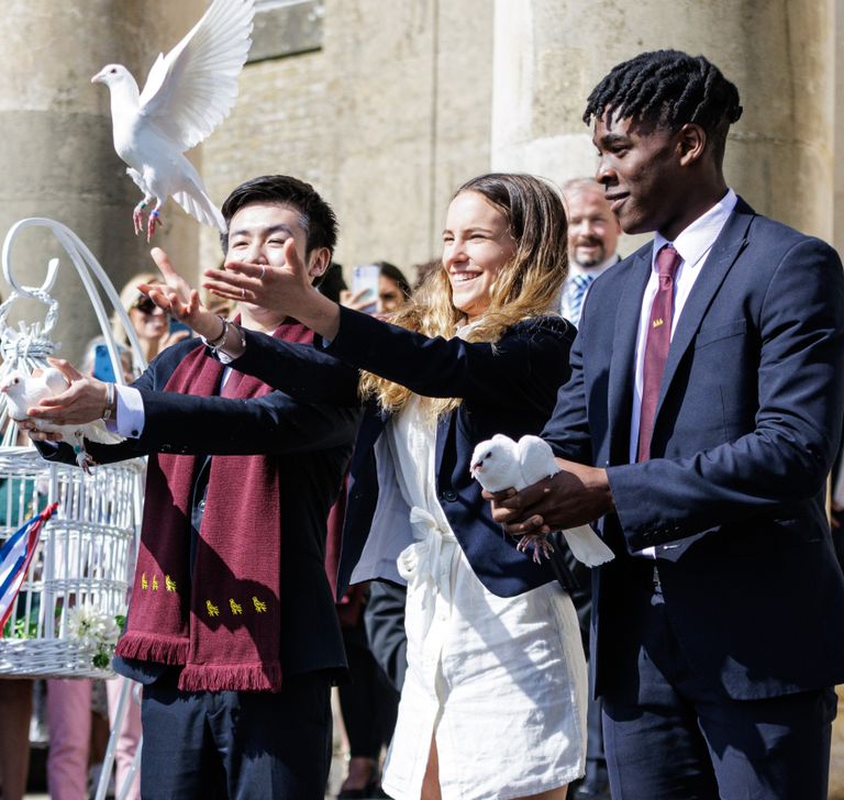Image of a young man holding out a dove, next to him a girl has let go of the dove and next to the girl a young man holding a dove  