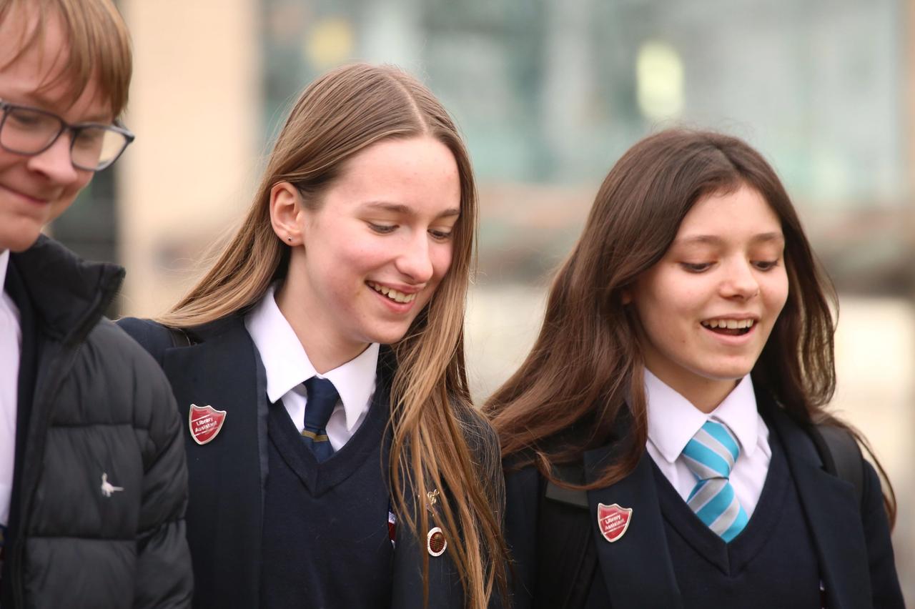 3 students smiling with their eyes looking down 