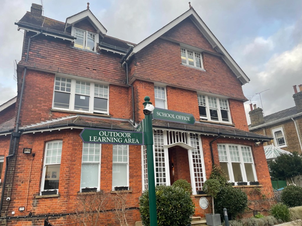 Image taken at Lyonsdown school of a building and a signpost with the visible signs of "outdoor learning area" and "school office"