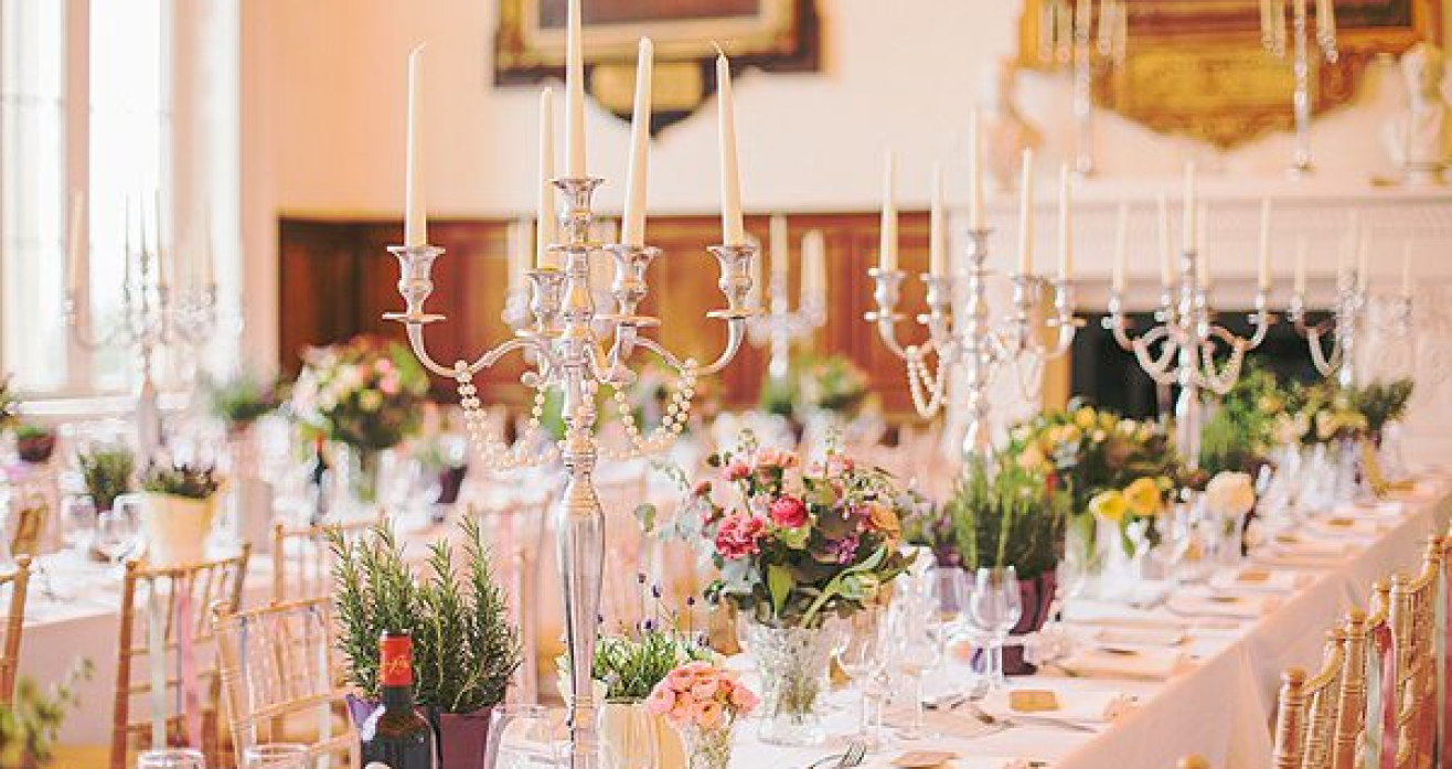 Two long tables set for dining with floral arrangements and candles 