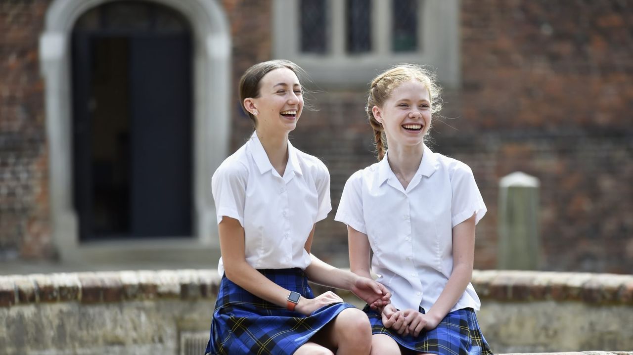Two girls from Cobham Hall School sitting down and laughing outside 