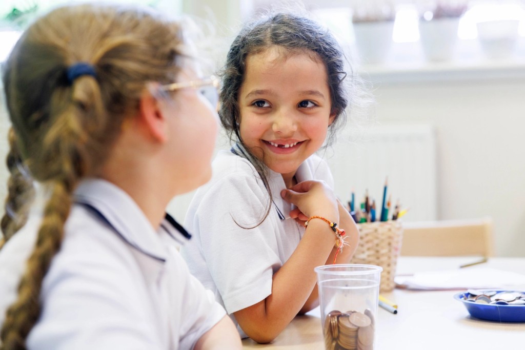A smiling little girl facing another little girl in a classroom