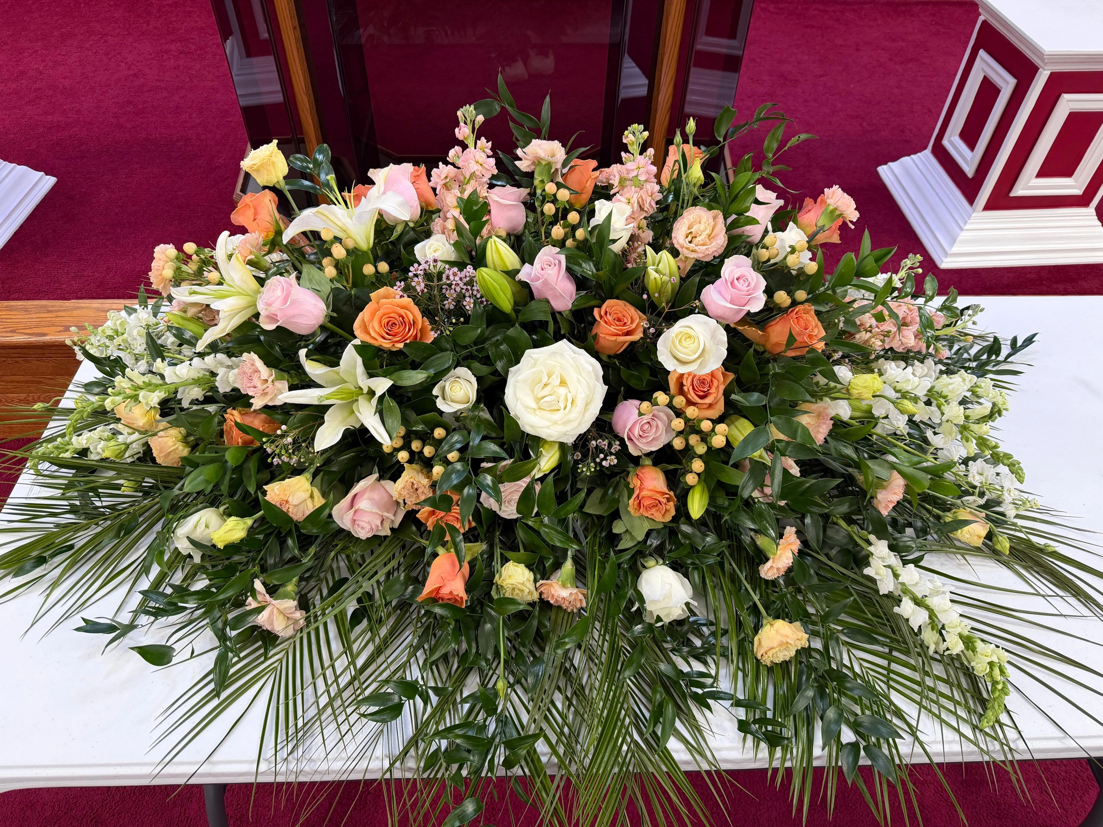 Medium sized casket spray with lots of greenery, and peach/pink florals