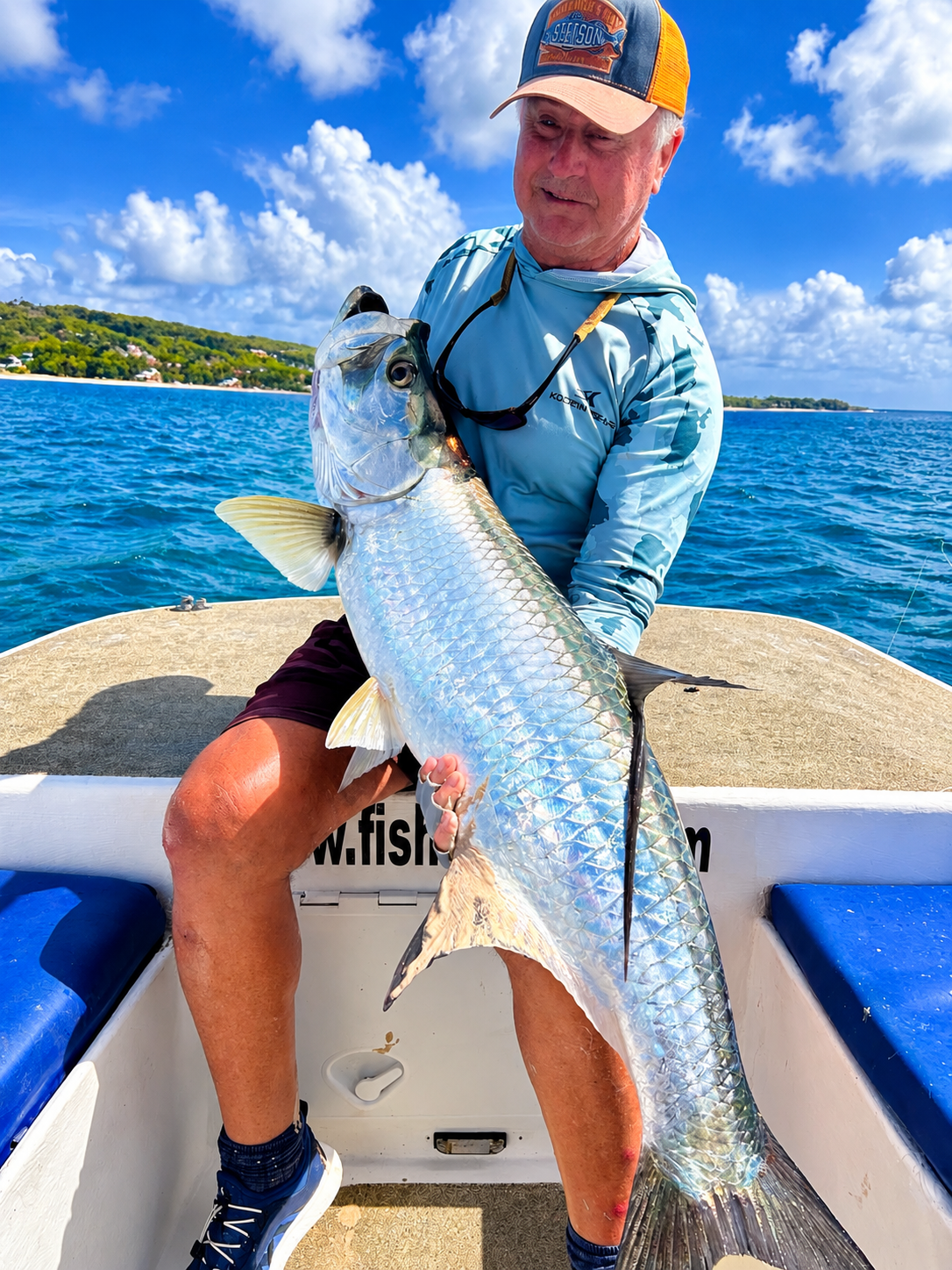 A crew member holding a mahi mahi up on the gaff, rods in the holders behind