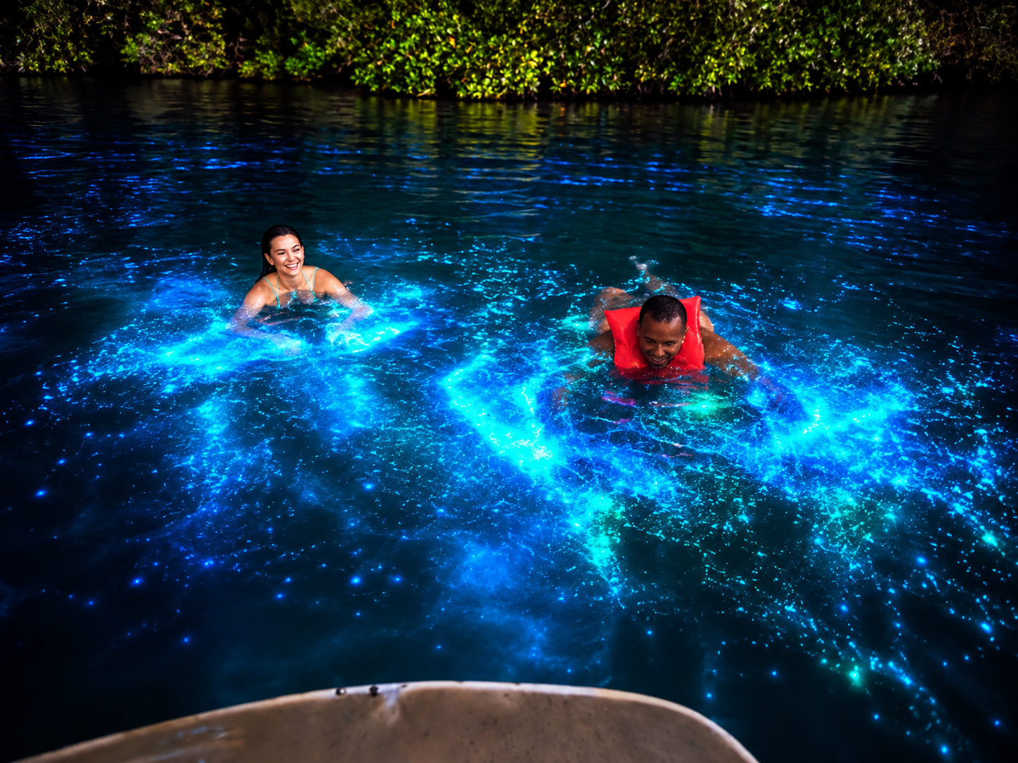 Swimmers ringed by glowing blue water in the lagoon at night
