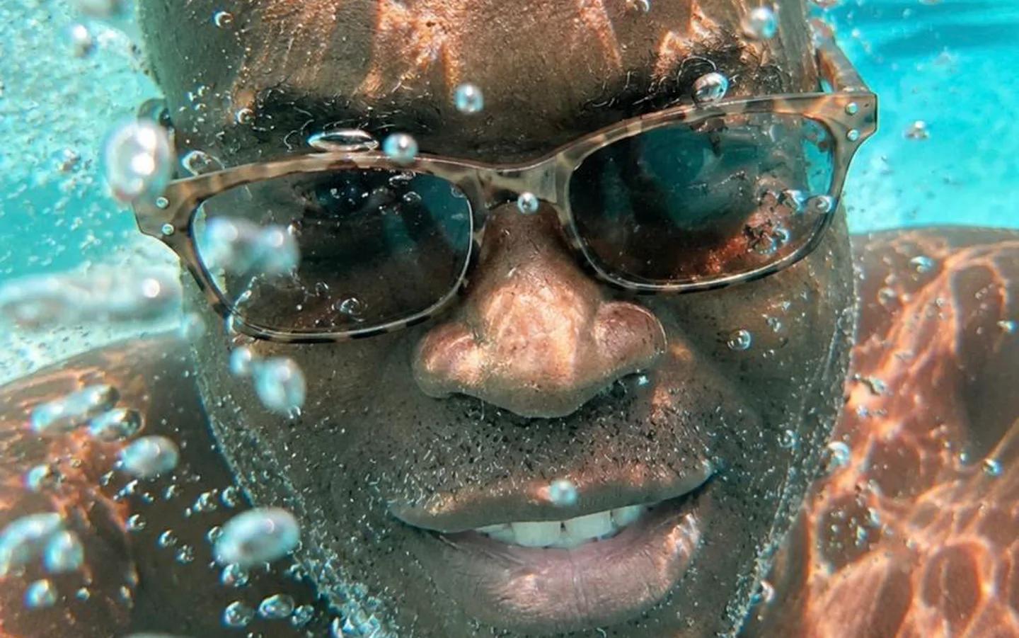 A snorkeler grinning underwater through a stream of bubbles