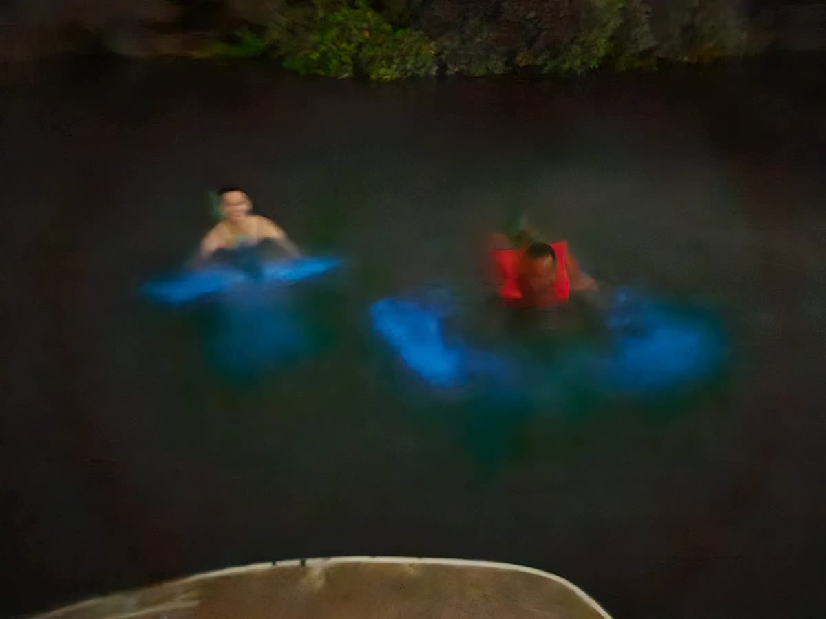 Two swimmers in the lagoon at night surrounded by glowing water