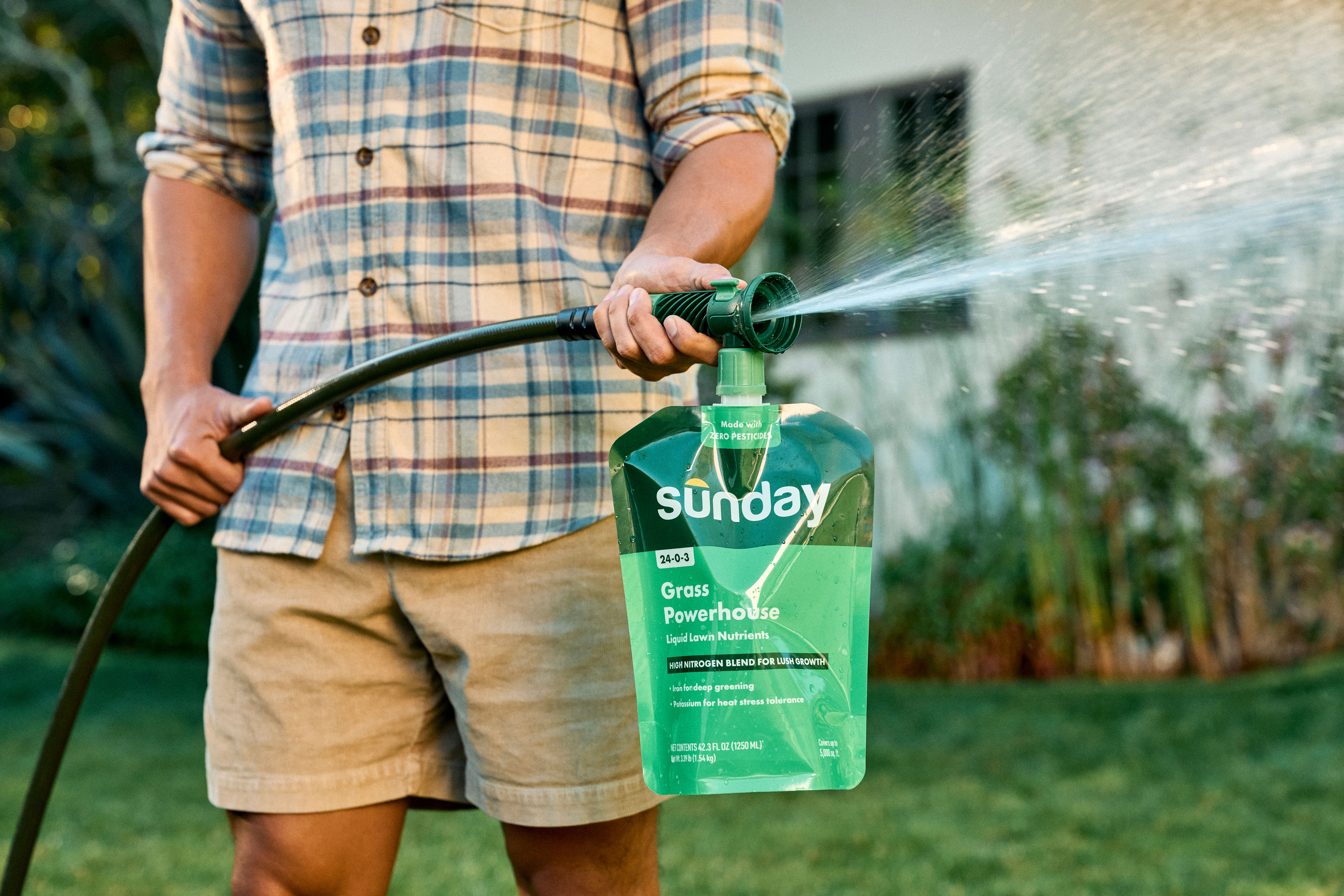 Person spraying Sunday Grass Powerhouse liquid lawn nutrients with a hose end sprayer in a backyard.