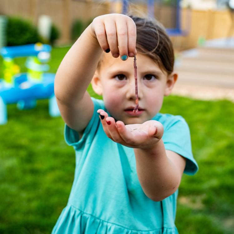 Child holding a worm in front of their face