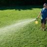 Person spraying Sunday Liquid Fertilizer on a green lawn with a hose end sprayer