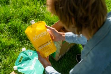 Person holding liquid lawn fertilizer pouch from Sunday Custom Lawn Plan.