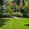 Sunny backyard with a bird feeder on a pole, green grass, and garden beds for pollinators.