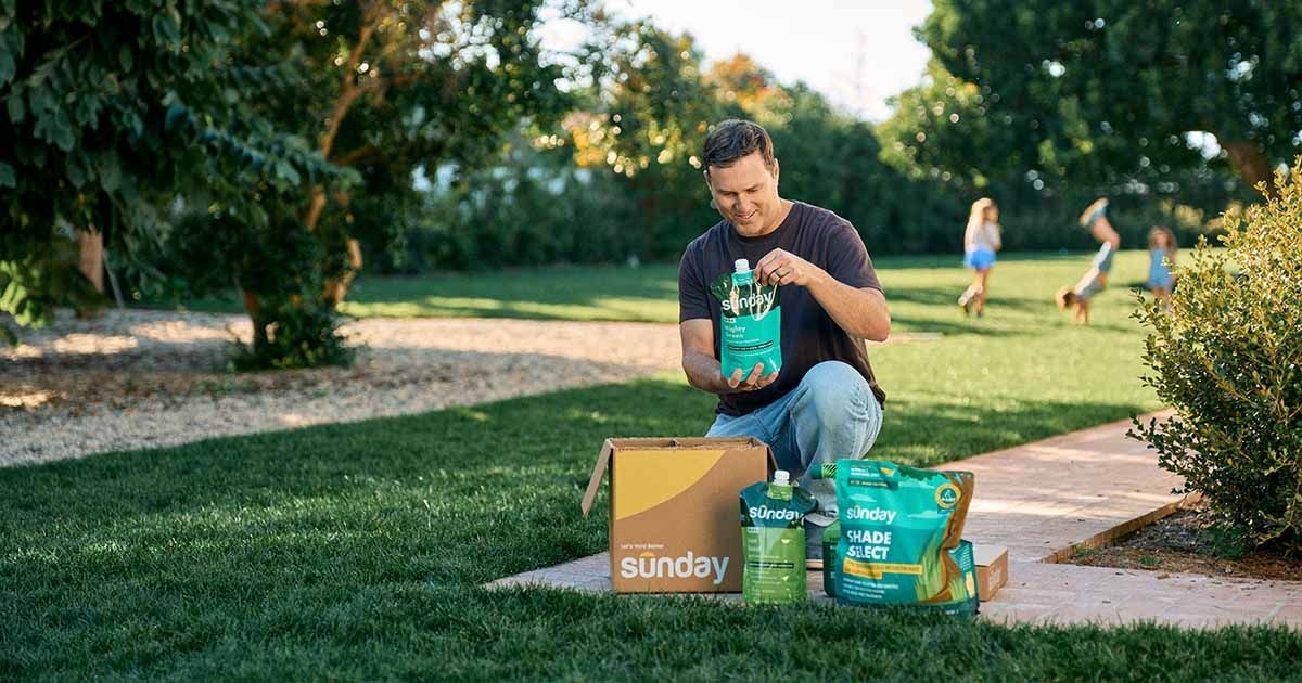 Person opening Sunday subscription box in his yard, children playing in the background