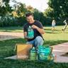 Person opening Sunday subscription box in his yard, children playing in the background