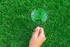 A hand holding a magnifying glass over grass