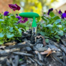 Garden soil test kit coring tool placed in soil and mulch of garden bed with plants