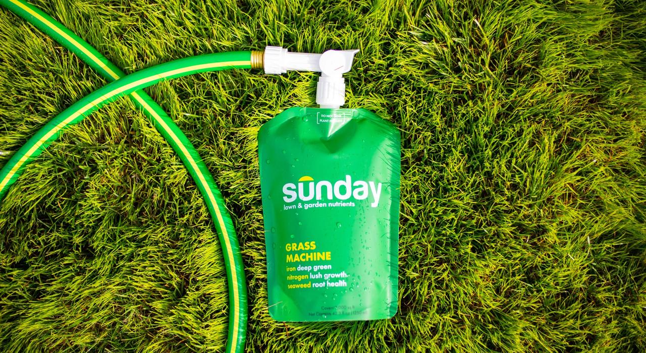 Sunday fertilizer pouch on grass with lawn mower next to it