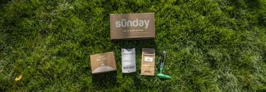 Sunday soil test kit items arranged on grass: shipping box, kit packet, return mailer, soil sample bag, and green soil corer.