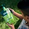 Person holding a Sunday Active Lawn liquid fertilizer pouch with a hose end sprayer attached, standing on a green lawn.